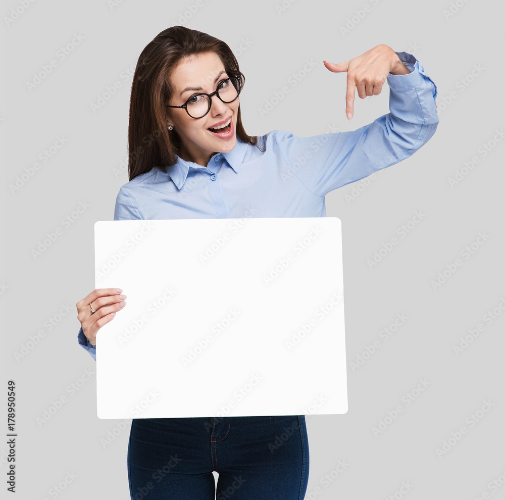 Happy young woman holding blank white banner and pointing at it Happy young woman holding blank white banner and pointing at it