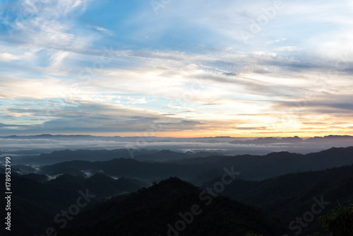 Mountain forest landscape under sunrise sky with clouds.