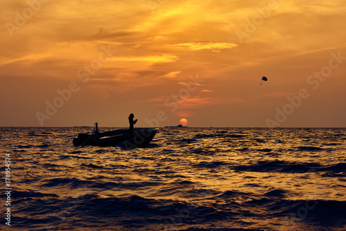 Silhouette of man in boat and parachute in sky against the golden sunset. © Dmitry Yakovtsev