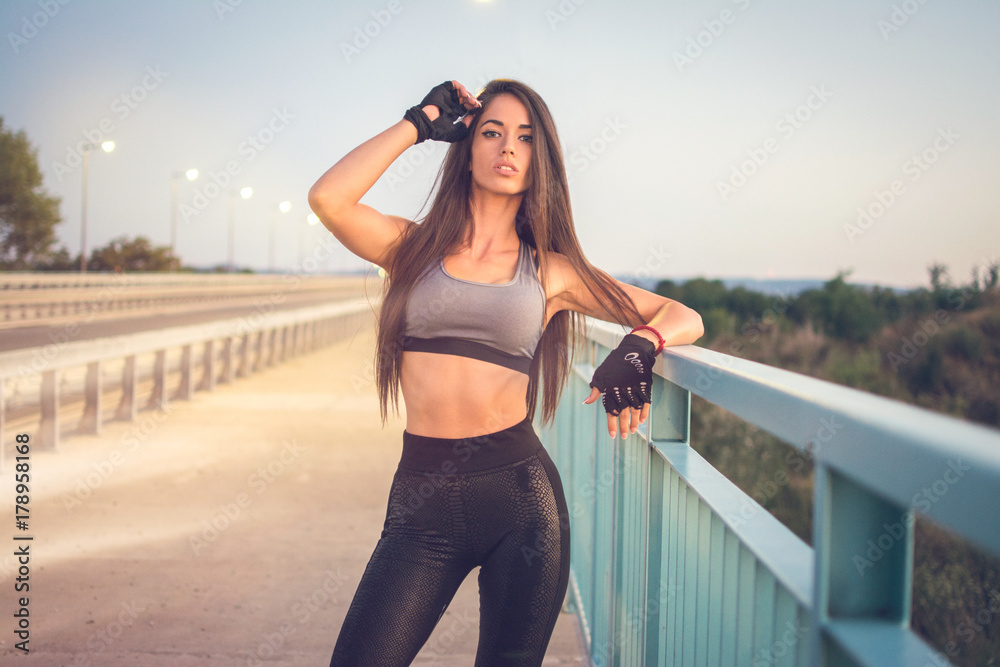 Portrait of sensual young woman in sportswear posing on bridge.