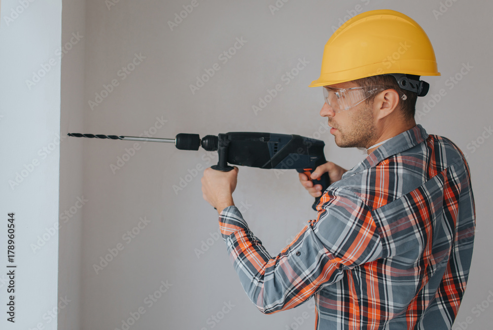 Builder worker with equipment making hole in wall at construction site Builder worker with equipment making hole in wall at construction site