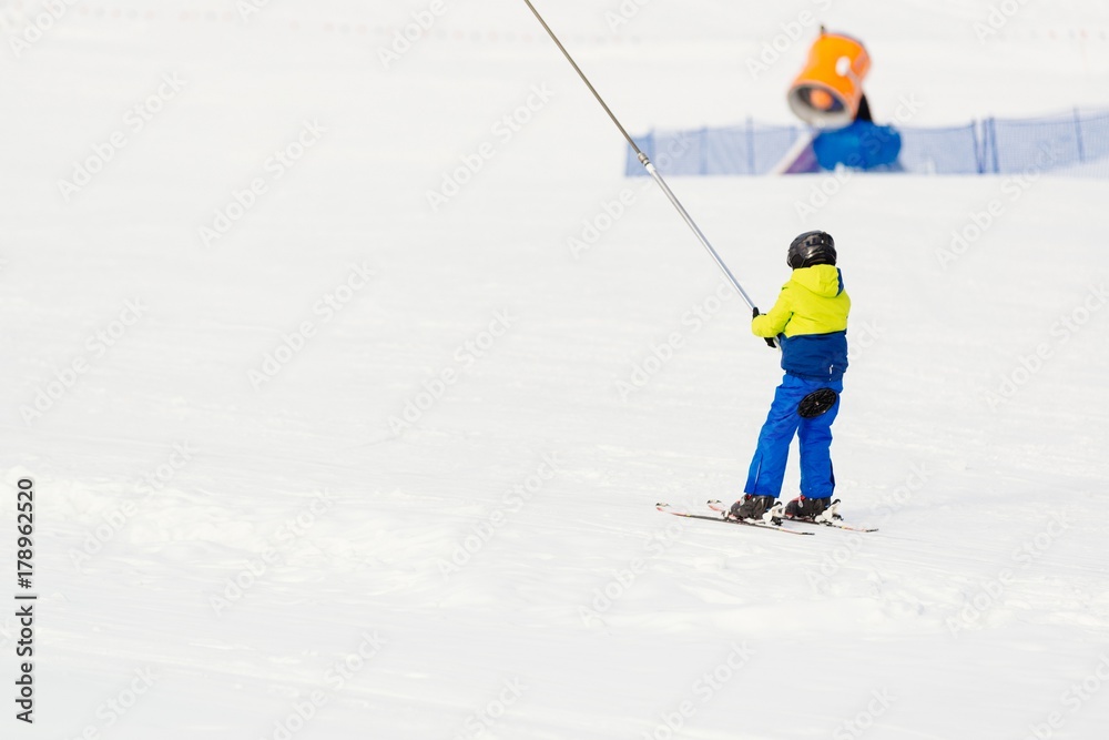 Little child going up the ski slope on ski lift.