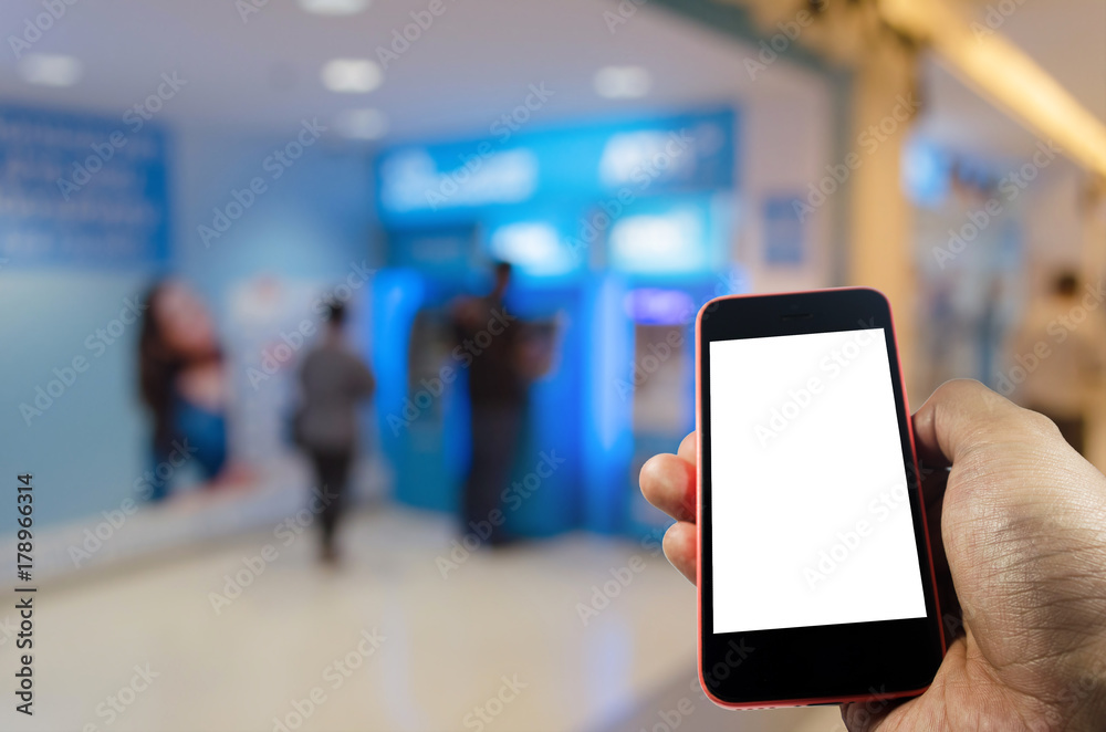 hand holding mobile phone with blank screen for e-banking text with people queuing to withdraw money from ATM banking machine in background, internet, financial, payment and shopping online concept hand holding mobile phone with blank screen for e-banking text with people queuing to withdraw money from ATM banking machine in background, internet, financial, payment and shopping online concept