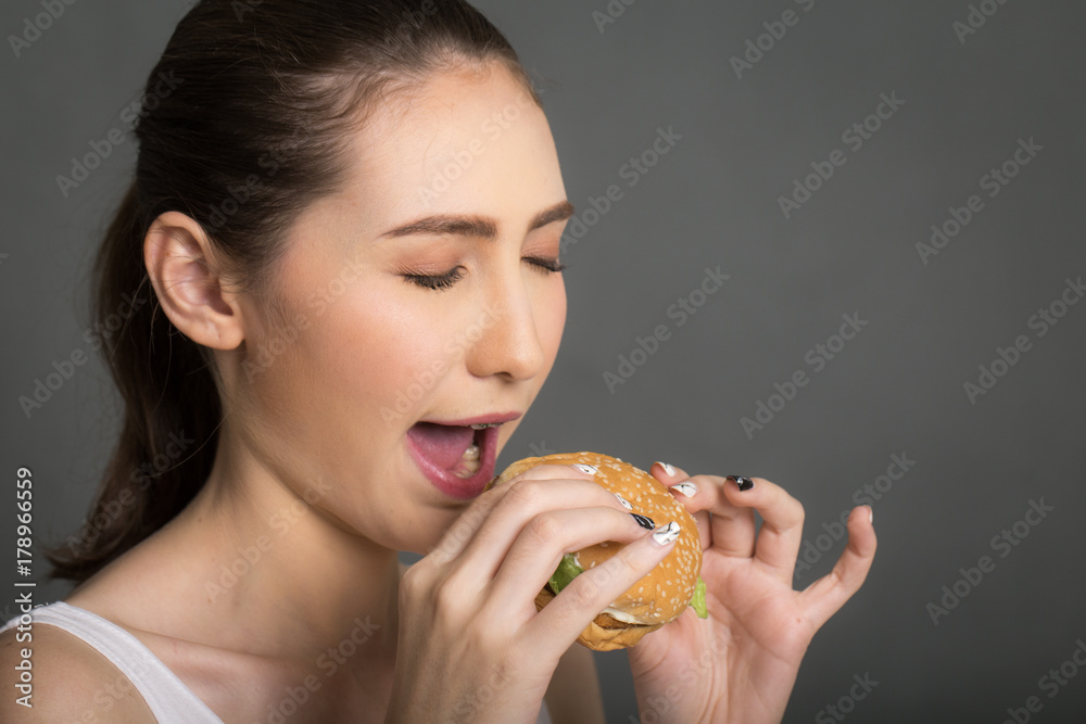 A woman eating burger isolated on gray balckgroung