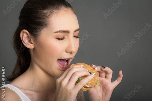 A woman eating burger isolated on gray balckgroung