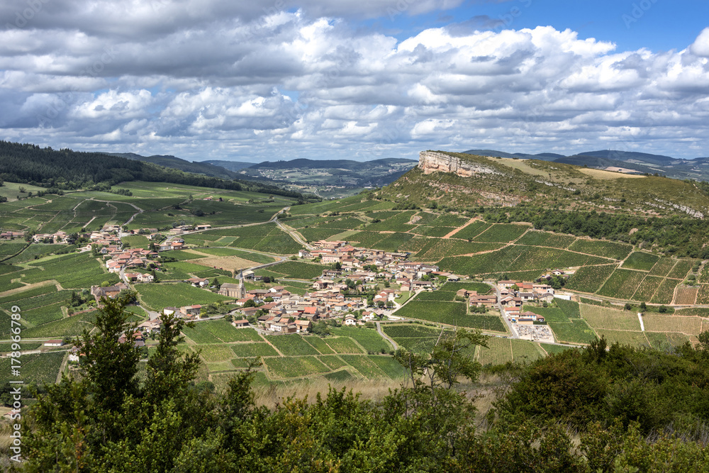 France; Solutre-Pouilly: Panoramic view with French town, Rock of Solutre on horizon, green vineyards, trees and cloudy blue sky - scenery
