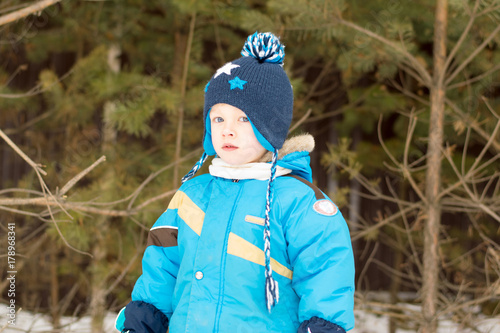 Obraz na płótnie A child boy takes a walk in a winter forest (park) interested in twigs w salonie
