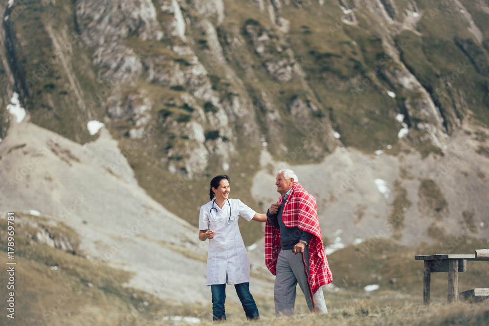 Nurse helping elderly senior man to walk on frash air outdoor.