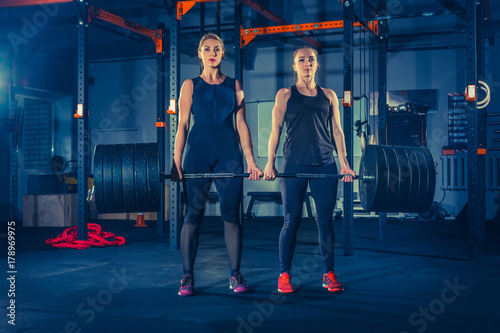 Fit young women lifting barbells and working out in a gym