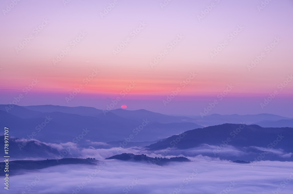 The top view of the silhouettes and peaks of the mountains at dawn, sunset, the rising sun from behind the mountains, a beautiful dawning colorful sky. Lovely mountain spacious landscape.
