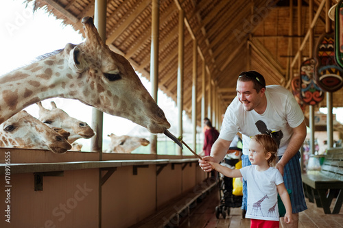 Photography Little kid boy with his dad  watching and feeding giraffe in zoo
