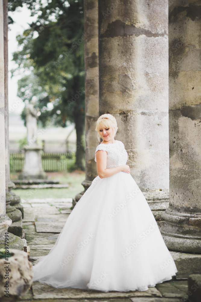 Beautiful elegant bride with perfect wedding dress and bouquet posing near old castle