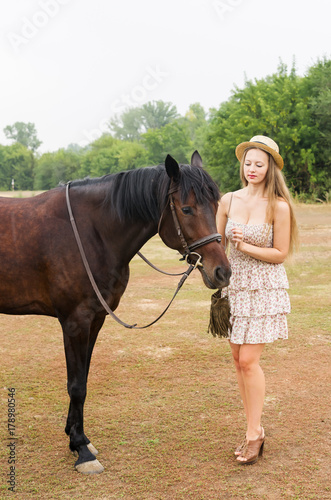 Beautiful girl in a straw hat and summer dress with a horse / Photographed in Russia, at the racetrack in Orenburg