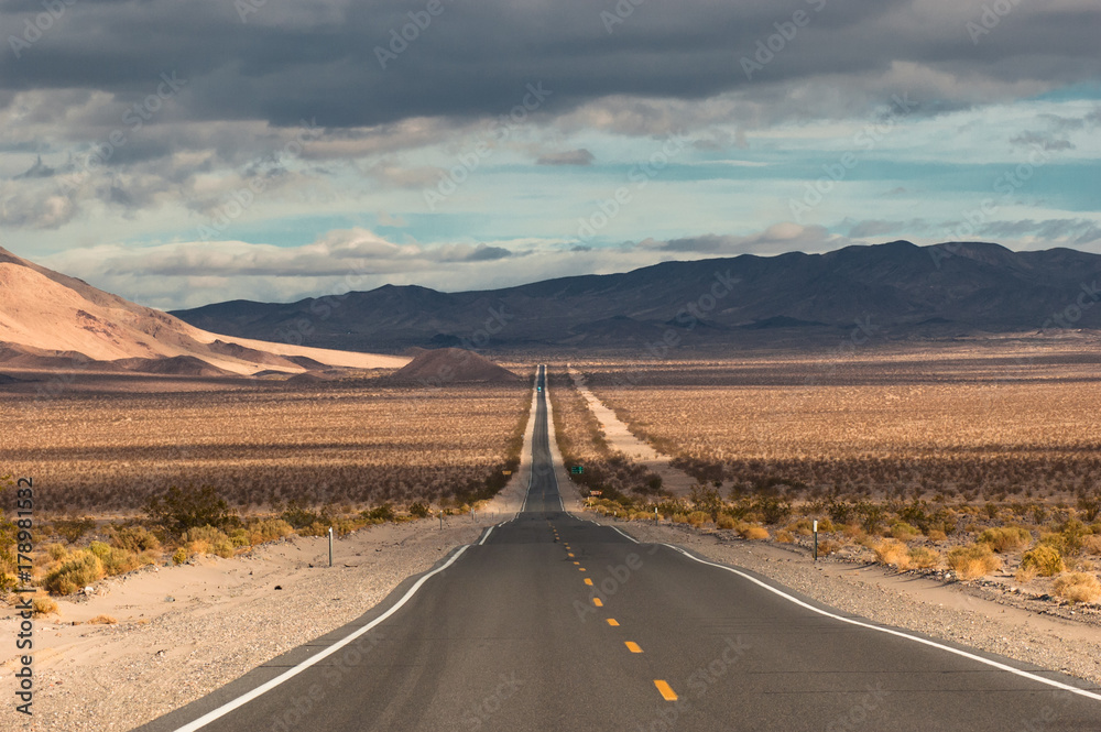 Classic long desert highway leading into the wild desert landscape of Death Valley National Park