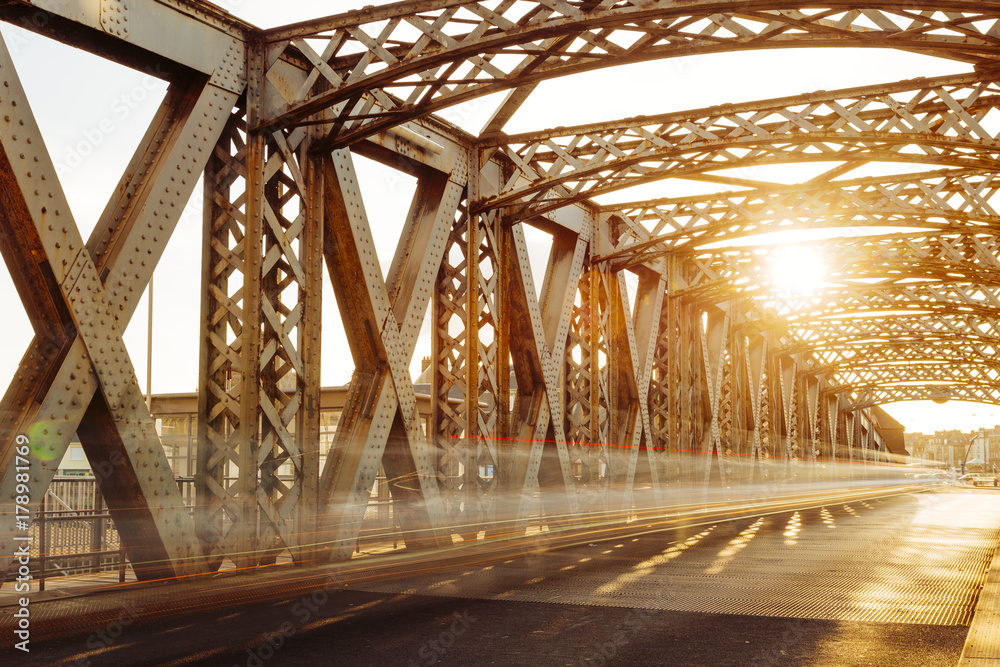 Asphalt road under the steel construction of a city bridge on a sunny day. Urban scene in the bridge tunnel. Long exposure. Toned Asphalt road under the steel construction of a city bridge on a sunny day. Urban scene in the bridge tunnel. Long exposure. Toned