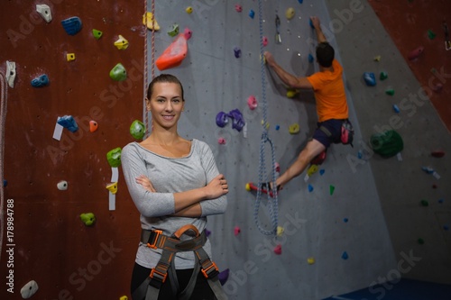 Portrait of confident athlete standing against man climbing wall