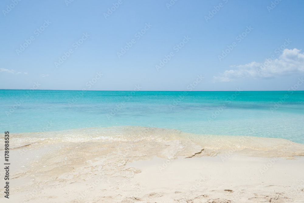 Turquoise sea water with white sand  rock beach and blue sky. Horizon line, Turks and Caicos Islands.