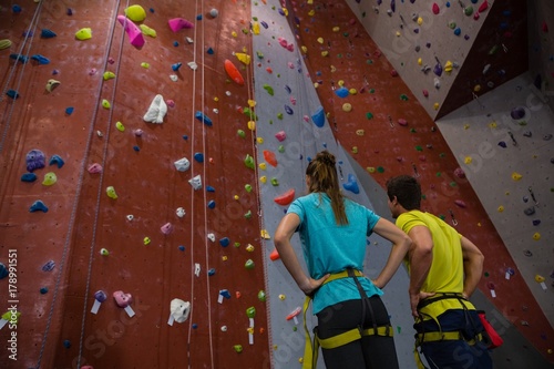 Athletes with hands on hip standing by climbing wall in gym