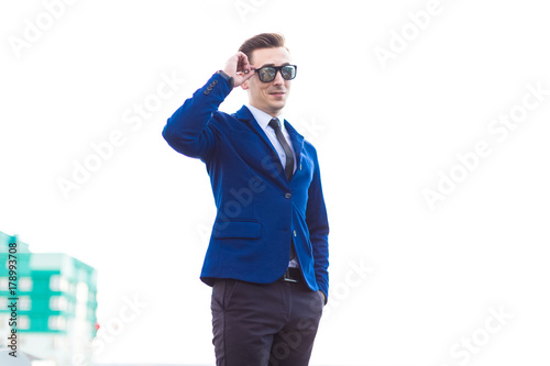 Attractive young busunessman in blue suit and sunglasses stand on the roof photo