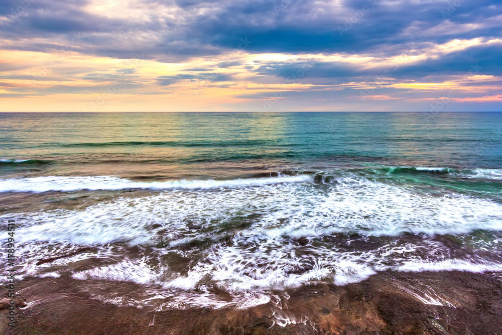 Obraz premium Foamy waves on a sunset background in cloudy weather with thunderclouds. Coastline of Tanah Lot, Beraban, Bali, Indonesia.