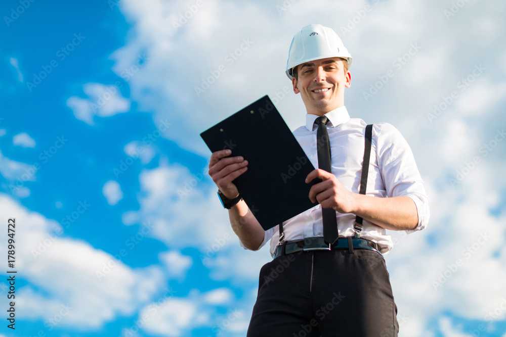 Young attractive foreman in white helmet, tie and braces stand on the roof with tablet Young attractive foreman in white helmet, tie and braces stand on the roof with tablet