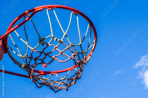Basketball hoop outdoors, closeup, low angle view. Red basketball hoop viewed from below against blue sky.