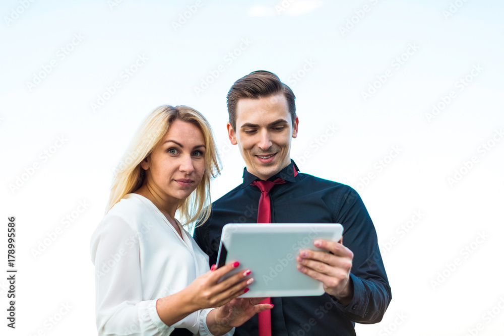 Couple of businessmen, good looking brunette man and attractive blonde woman stand on the roof and look in tablets Couple of businessmen, good looking brunette man and attractive blonde woman stand on the roof and look in tablets