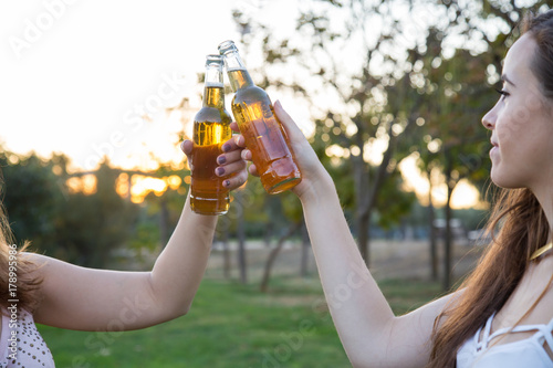 Close-up of two young women toasting with beer bottles having fun. 