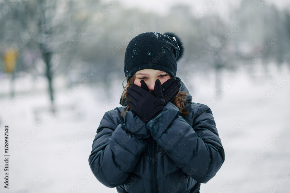 girl covered mouth with gloves. The girl made a gesture, silence. A child walks after school on the street in a snowfall. girl covered mouth with gloves. The girl made a gesture, silence. A child walks after school on the street in a snowfall.