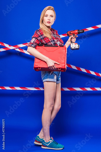 Attractive sexy builder girl in red chechered shirt, jean shorts and snickers hold screwdriver and toolbox photo