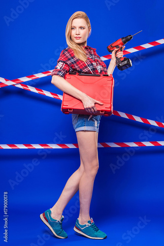 Attractive sexy builder girl in red chechered shirt, jean shorts and snickers hold screwdriver and toolbox photo