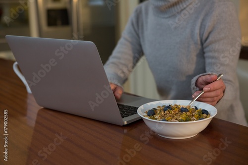Mid section of woman having breakfast while using laptop