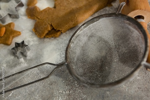 Stainer and cookie dough with flour on table photo