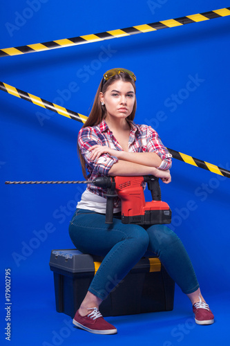 Pretty sexy worker girl in chechered shirt, build goggles and jeans sit on tool box with drill photo