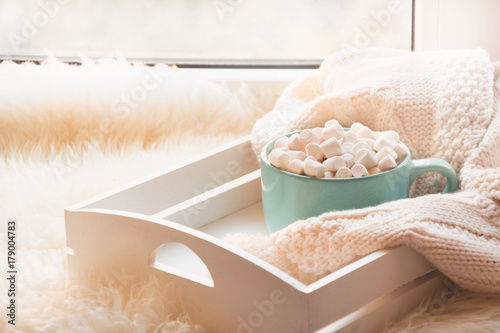Blue cup of hot chocolate with marshmallow on white windowsill with furskin for rest. Holiday. photo