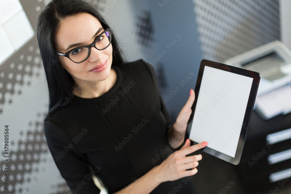 Beautiful young businesswoman in black dress and glasses hold paper folder and show tablet Beautiful young businesswoman in black dress and glasses hold paper folder and show tablet