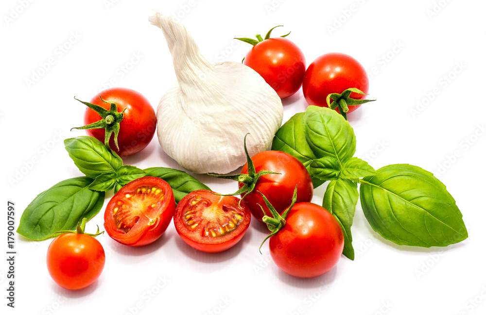 Group of whole fresh red cherry tomatoes, two cherry halves, fresh green basil leaves and one garlic in centre isolated on white background