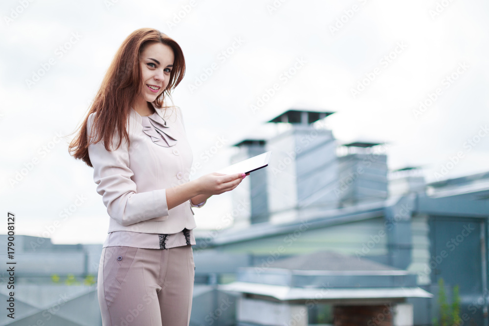 Pretty businesswoman in beige suit stand on the roof and hold empty tablet