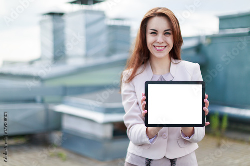 Pretty businesswoman in beige suit stand on the roof and hold empty tablet