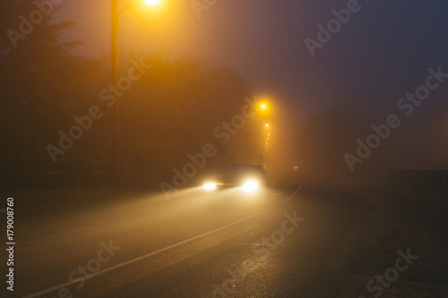 Country asphalt road in the region of Normandy  France in foggy day. Street lamps and car headlights at night. Toned