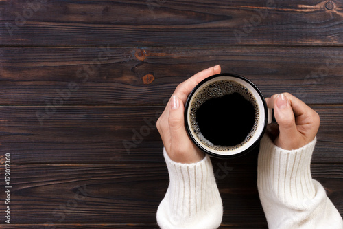 Lonely woman drinking coffee in the morning, top view of female hands holding cup of hot beverage on wooden desk
