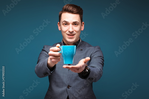Young handsome businessman in grey jacket and black shirt hold blue cup