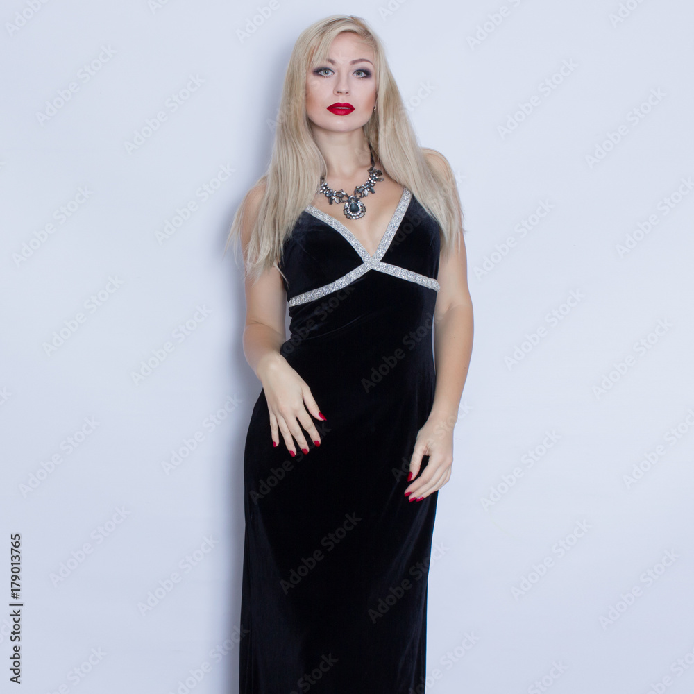 Beautiful blonde woman in black evening dress posing on grey background. Girl with black necklace Beautiful blonde woman in black evening dress posing on grey background. Girl with black necklace