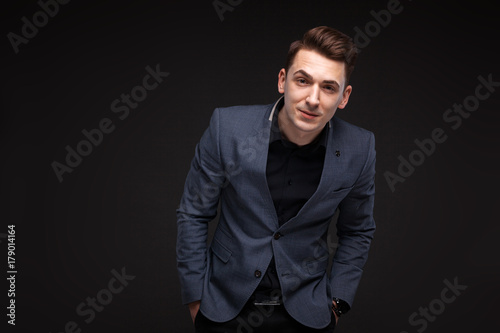 Young attractive businessman in grey jacket, costly watch and black shirt, black background
