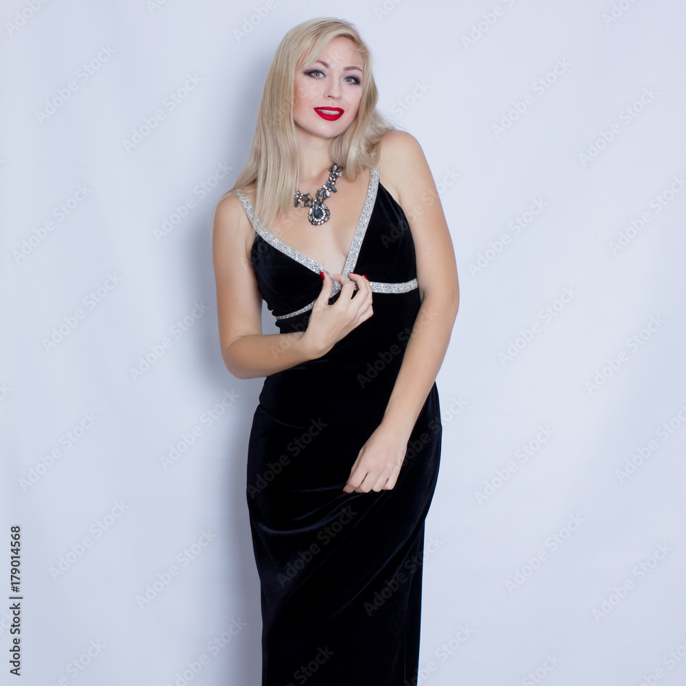 Beautiful blonde woman in black evening dress posing on grey background. Girl with black necklace Beautiful blonde woman in black evening dress posing on grey background. Girl with black necklace