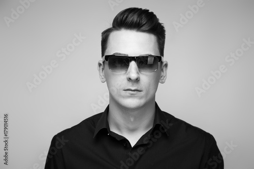 Handsome young businessman in costly watch, sunglasses and black shirt