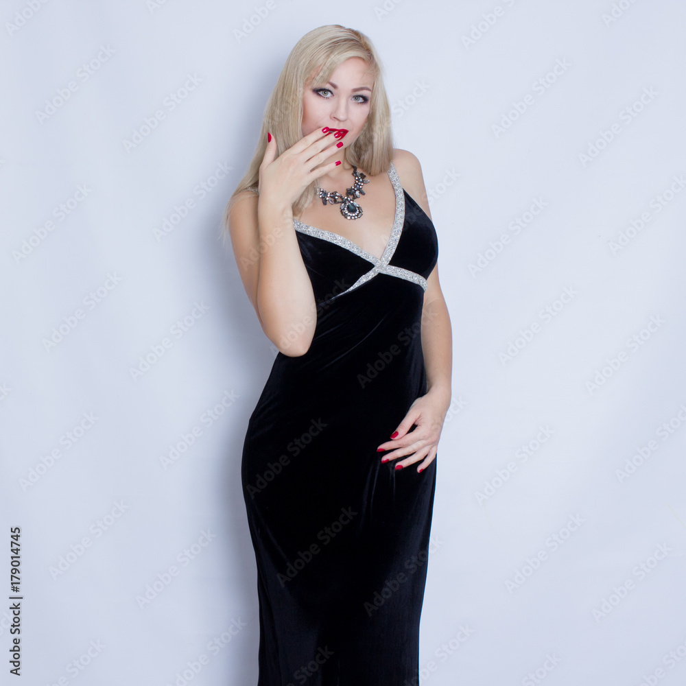 Beautiful blonde woman in black evening dress posing on grey background. Girl with black necklace Beautiful blonde woman in black evening dress posing on grey background. Girl with black necklace