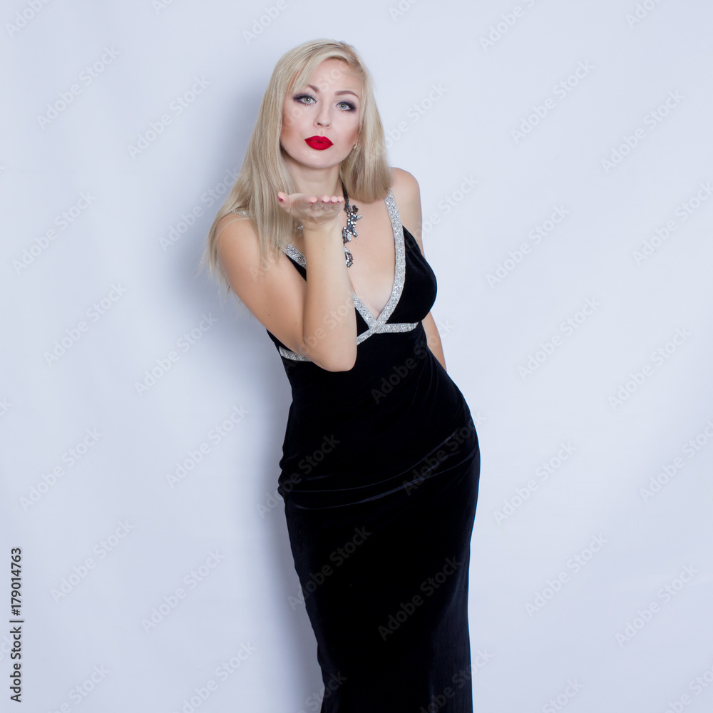 Beautiful blonde woman in black evening dress posing on grey background. Girl with black necklace Beautiful blonde woman in black evening dress posing on grey background. Girl with black necklace