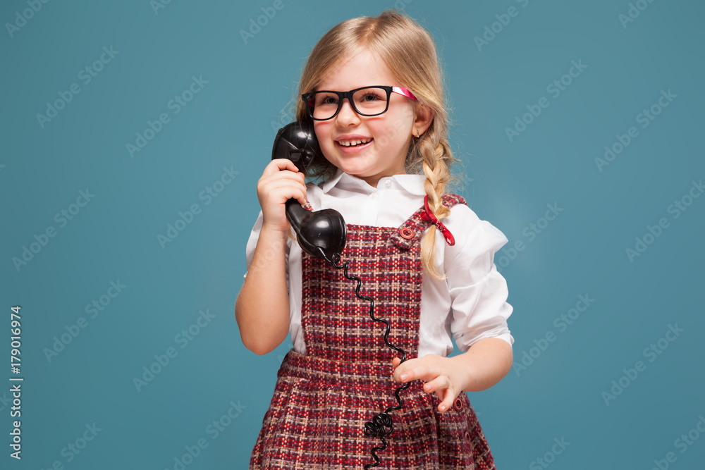Obraz premium Adorable little girl in red dress, white shirt and glasses holds phone handset