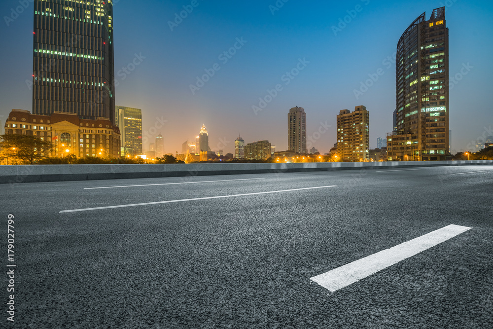 Empty asphalt road and illuminated modern cityscape background at night
